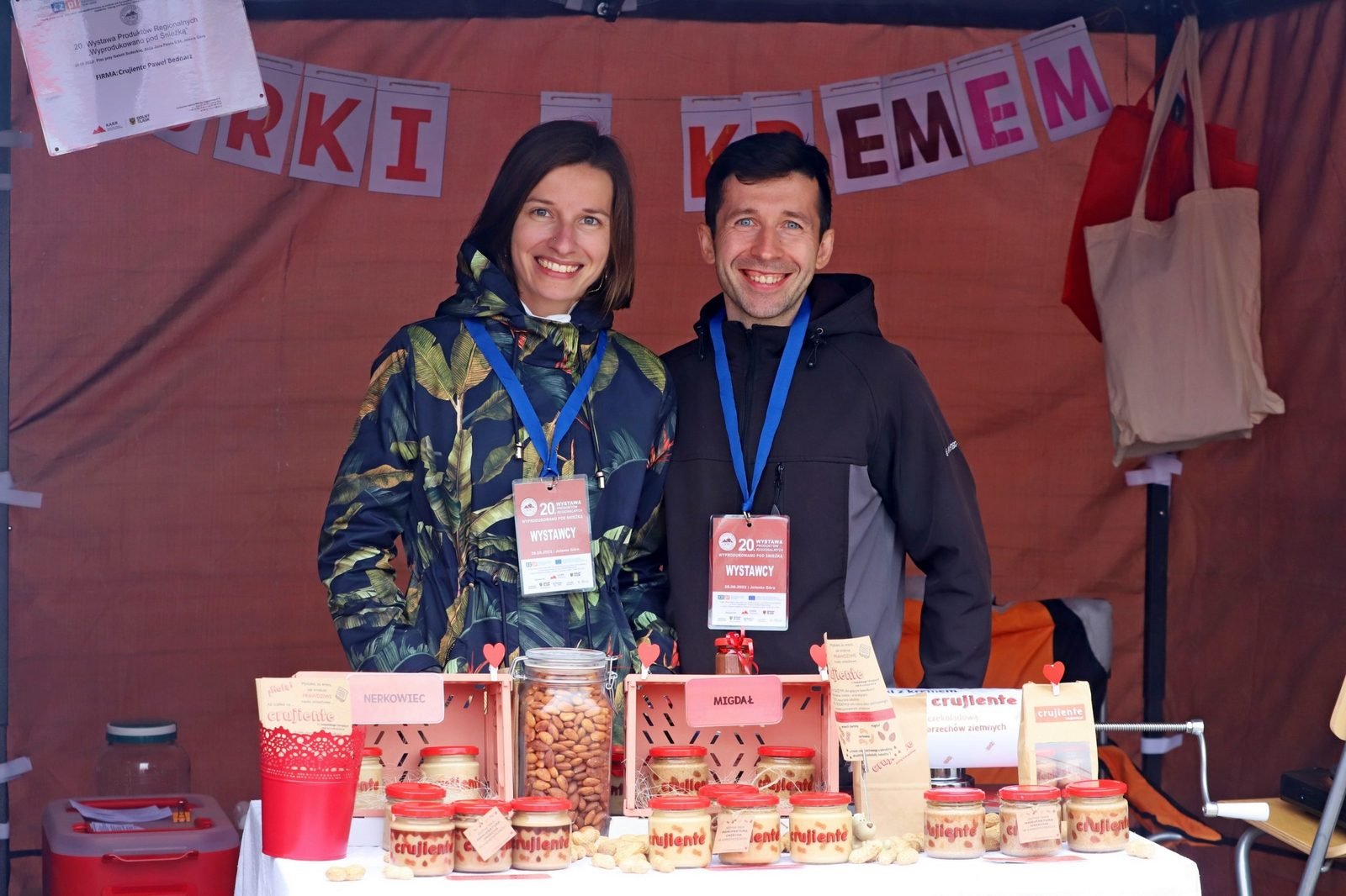 Paweł i Magdalena za stoiskiem Crujiente, w tle dyplom nagrody, na stole słoiki past