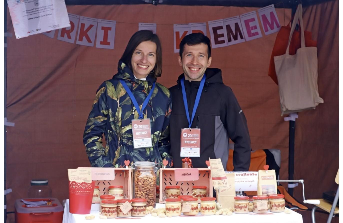 Magdalena i Paweł z identyfikatorami wystawców na 20. Wystawie Wyprodukowano pod Śnieżką, przed nimi skrzynki z orzechami i słoiki